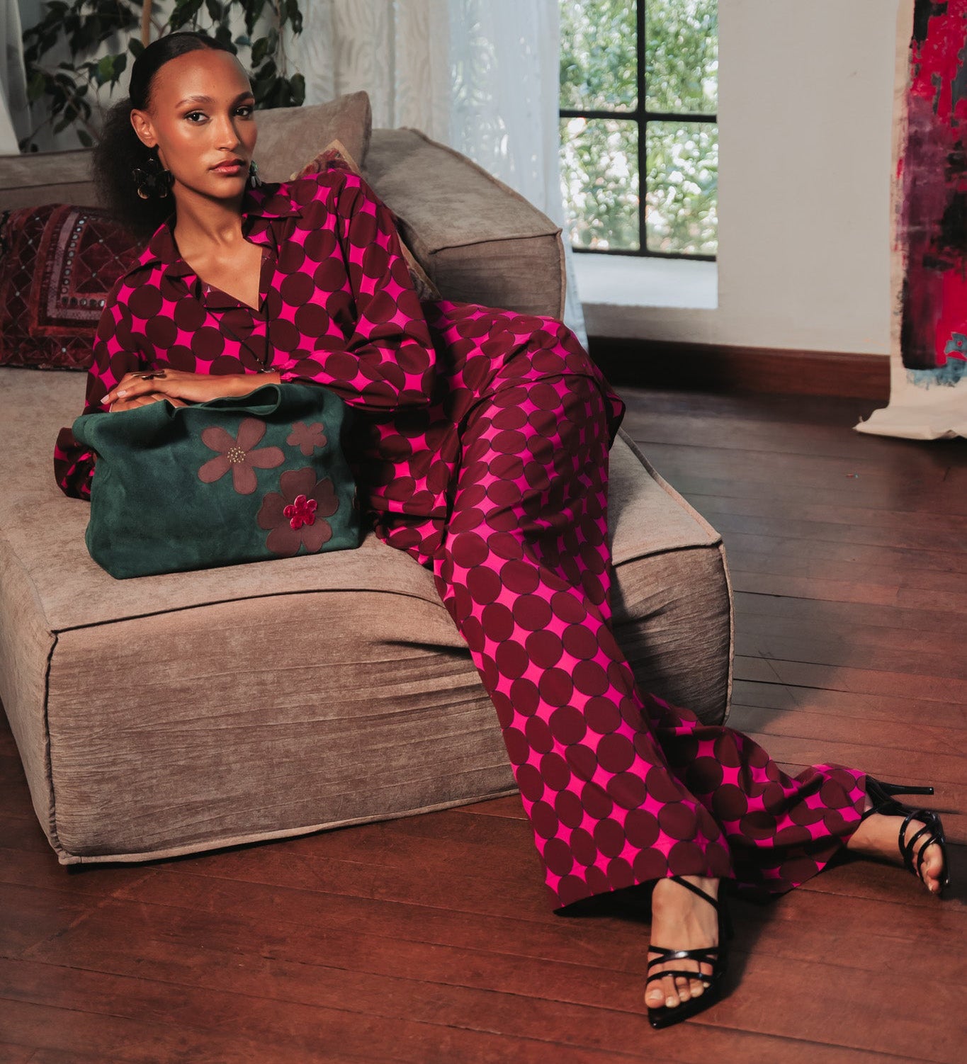 Woman in a pink and red patterned outfit sitting on a couch holding a green bag.